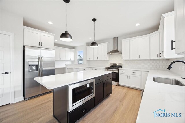 kitchen with a sink, stainless steel appliances, wall chimney exhaust hood, and light countertops