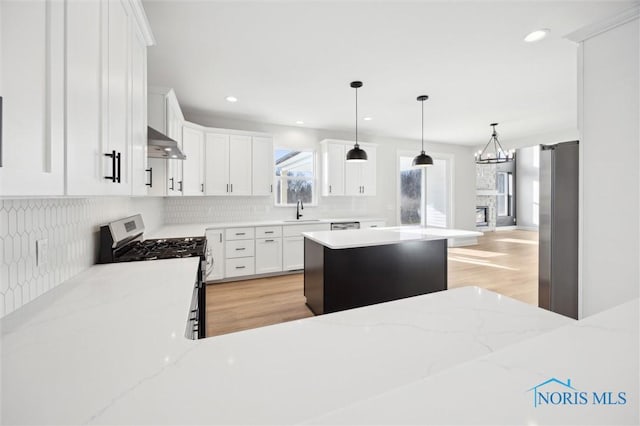 kitchen with backsplash, stainless steel range with gas cooktop, under cabinet range hood, white cabinets, and a sink