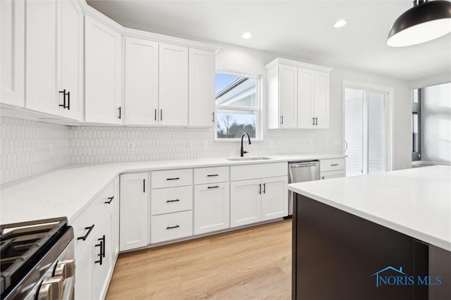 kitchen with a sink, backsplash, stainless steel appliances, white cabinets, and light countertops