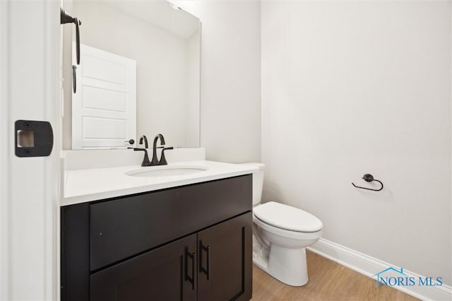 half bath with vanity, toilet, wood finished floors, and baseboards