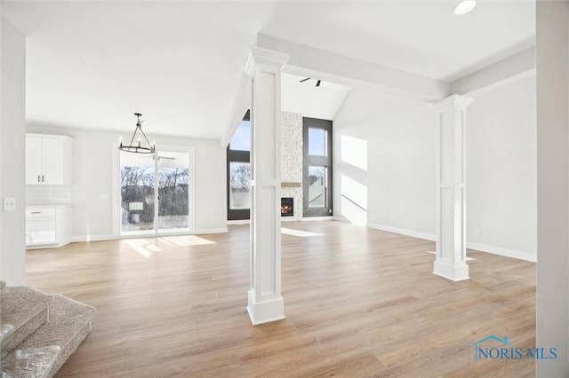 unfurnished living room with baseboards, a large fireplace, light wood-style flooring, and ornate columns