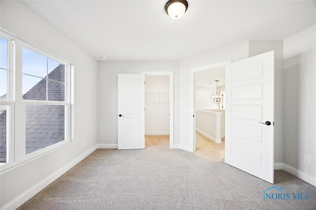 unfurnished bedroom featuring a walk in closet, a closet, baseboards, and carpet floors