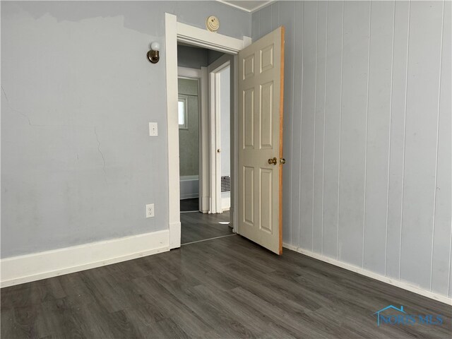 spare room with dark hardwood / wood-style flooring and wooden walls