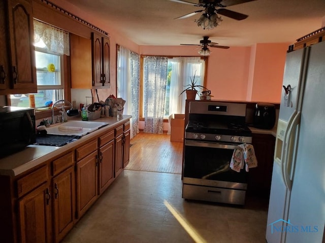 kitchen featuring white refrigerator with ice dispenser, light hardwood / wood-style floors, sink, ceiling fan, and stainless steel range with gas cooktop