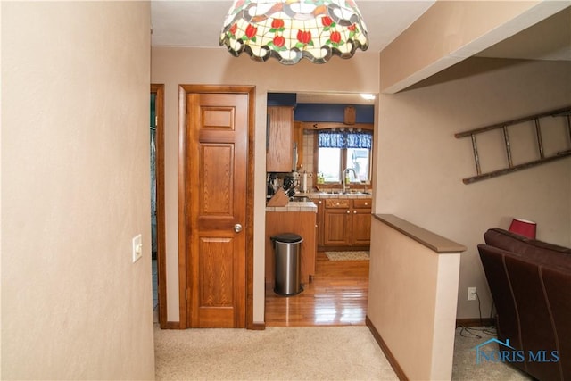 corridor with light carpet, a sink, and baseboards