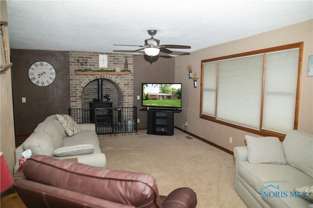 living room featuring ceiling fan, a textured ceiling, carpet floors, and a wood stove