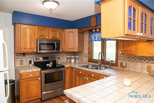 kitchen featuring tile countertops, stainless steel appliances, a sink, and glass insert cabinets