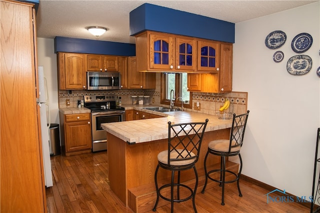 kitchen featuring decorative backsplash, dark hardwood / wood-style flooring, kitchen peninsula, appliances with stainless steel finishes, and a breakfast bar area