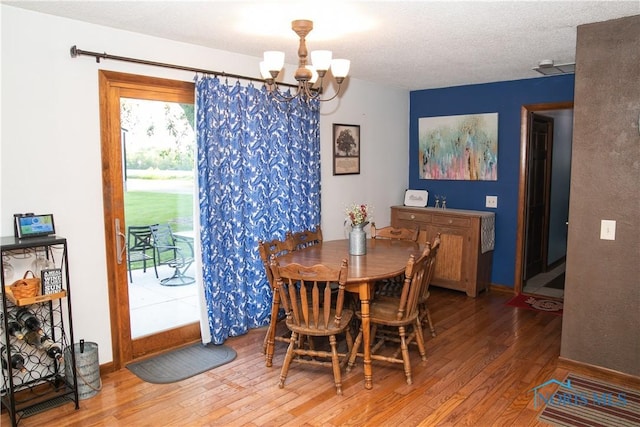 dining space featuring a textured ceiling, baseboards, wood finished floors, and a notable chandelier