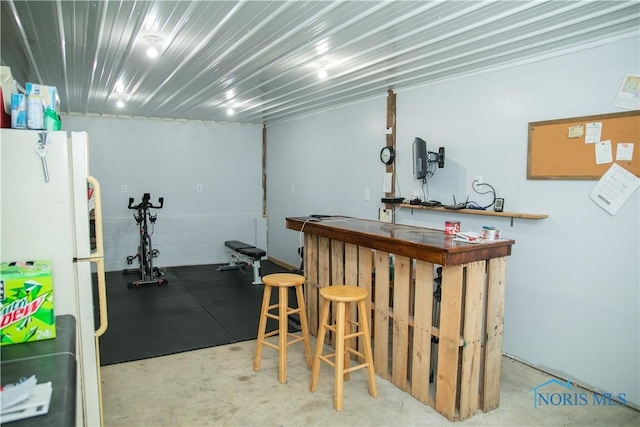 bar with freestanding refrigerator, concrete floors, and a dry bar