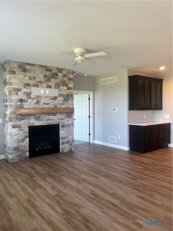 unfurnished living room with ceiling fan, dark hardwood / wood-style floors, and a stone fireplace