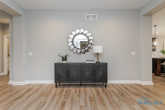 hall featuring light wood-style flooring, visible vents, and baseboards
