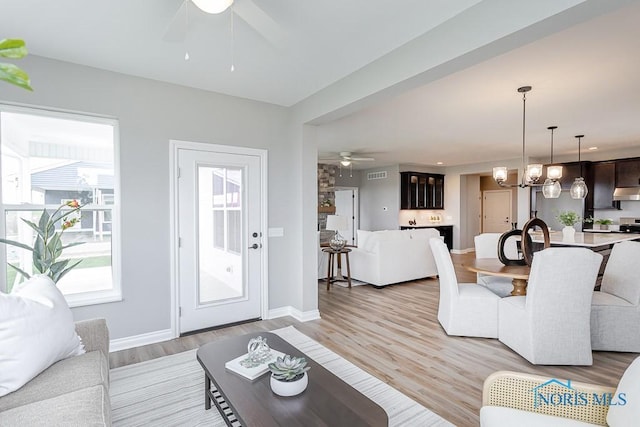 living area featuring baseboards, light wood-style floors, visible vents, and ceiling fan with notable chandelier