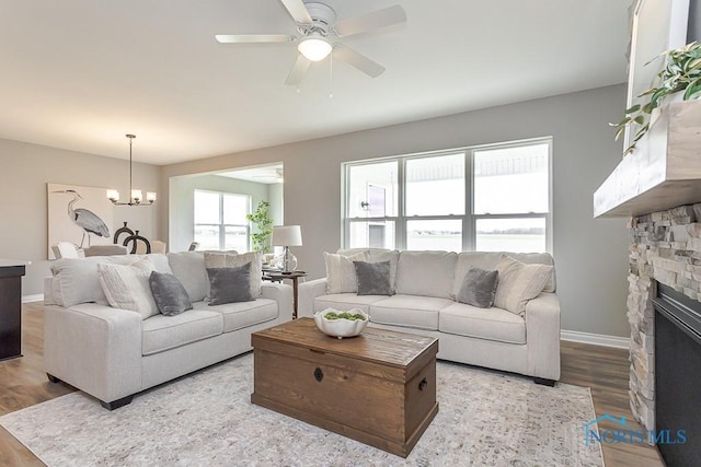 living area with ceiling fan with notable chandelier, baseboards, wood finished floors, and a fireplace