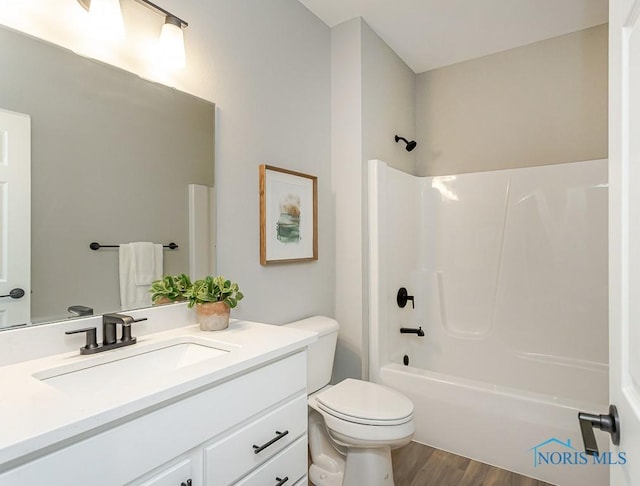 bathroom with toilet, vanity, wood finished floors, and  shower combination