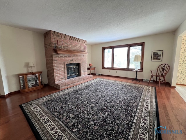 living room with hardwood / wood-style flooring, a textured ceiling, a brick fireplace, and brick wall