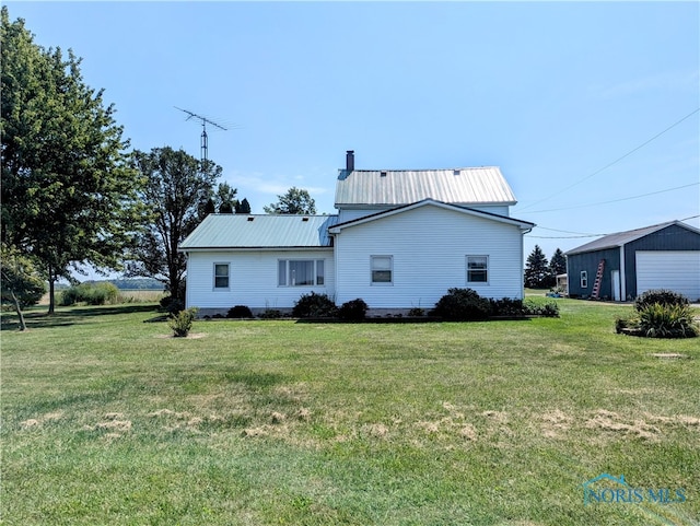 rear view of property featuring a yard, a garage, and an outbuilding