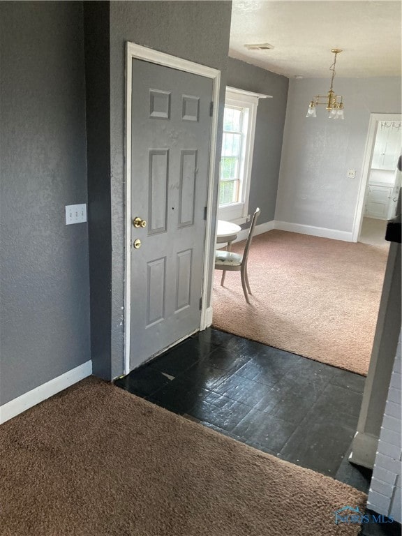 entryway with an inviting chandelier and dark carpet