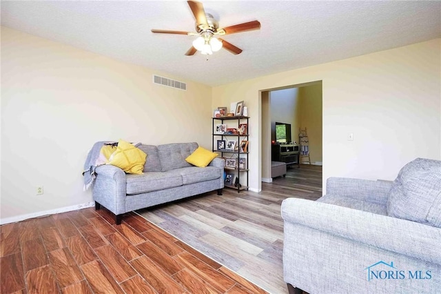 living room with visible vents, baseboards, ceiling fan, a textured ceiling, and wood finished floors