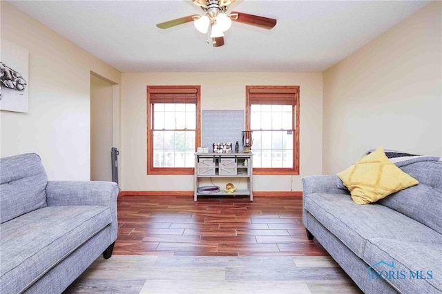 living area featuring baseboards, a ceiling fan, and wood finished floors