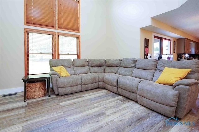 living area with a towering ceiling, visible vents, baseboards, and light wood-style flooring