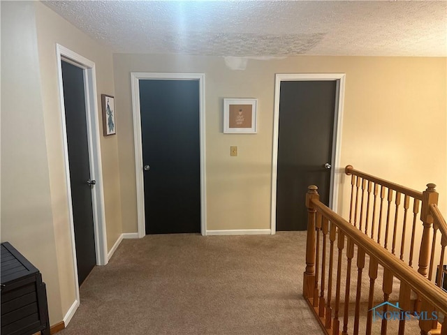hallway with a textured ceiling, baseboards, an upstairs landing, and carpet floors
