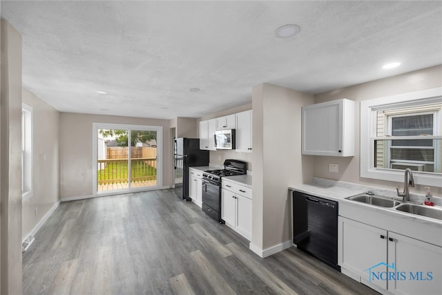 kitchen featuring black appliances, hardwood / wood-style flooring, white cabinets, and sink