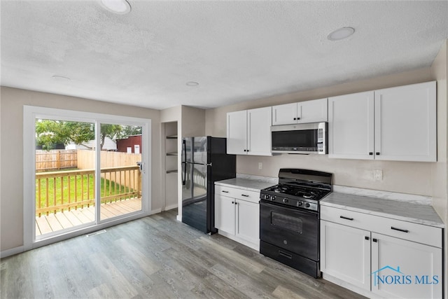 kitchen with light wood-type flooring, white cabinetry, a textured ceiling, black appliances, and light stone countertops