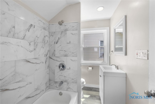 full bathroom featuring hardwood / wood-style flooring, vaulted ceiling, toilet, tiled shower / bath combo, and vanity