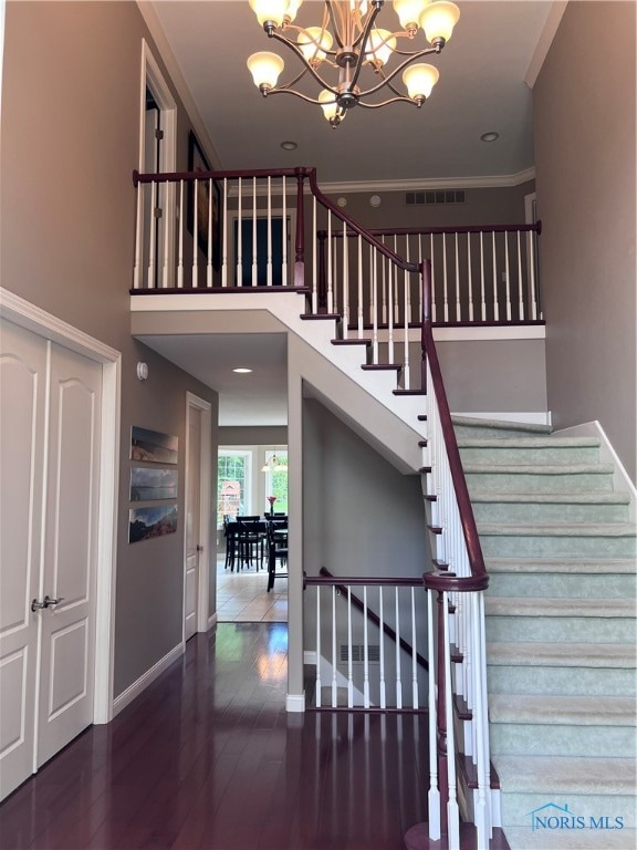 stairs with a chandelier, hardwood / wood-style floors, and crown molding