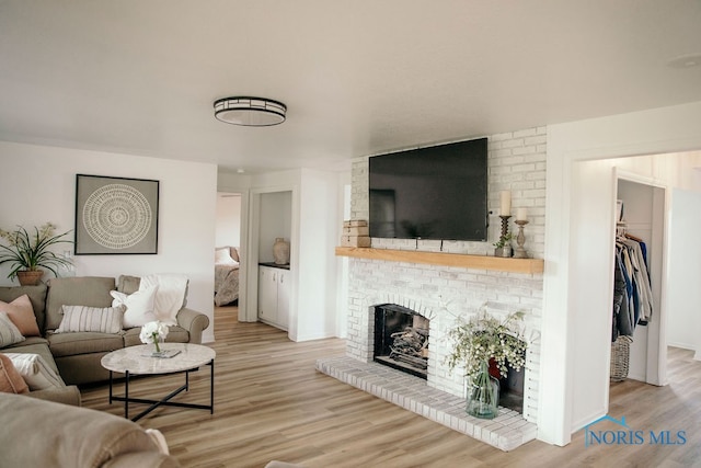 living room featuring brick wall, light hardwood / wood-style flooring, and a fireplace