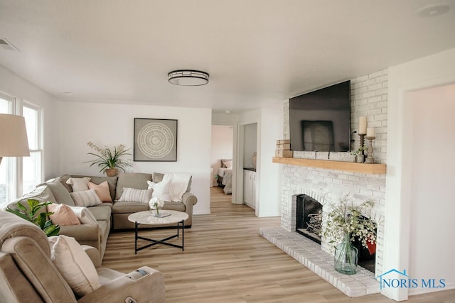 living room featuring light wood-type flooring, brick wall, and a brick fireplace