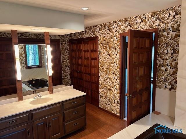 bathroom with a tub to relax in, wallpapered walls, wood finished floors, and vanity