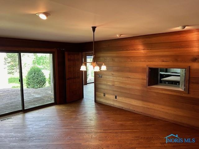 unfurnished dining area featuring an inviting chandelier, wood-type flooring, and wooden walls