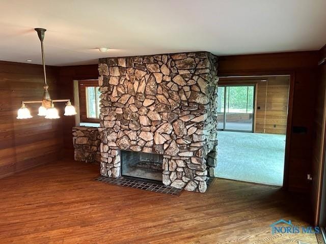 unfurnished living room with a notable chandelier, wood walls, a stone fireplace, and wood finished floors
