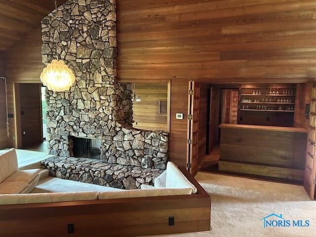 carpeted living room with vaulted ceiling, wood walls, and a stone fireplace