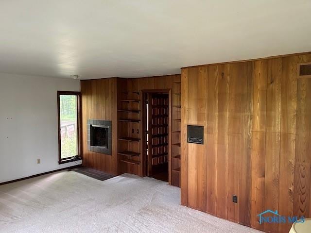 unfurnished living room featuring light carpet, a fireplace, and wooden walls