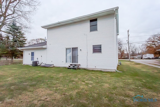 rear view of house featuring central air condition unit and a lawn