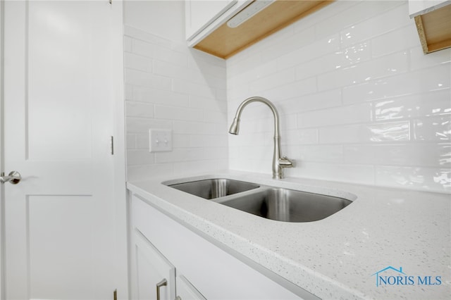 room details featuring sink, light stone countertops, and white cabinetry