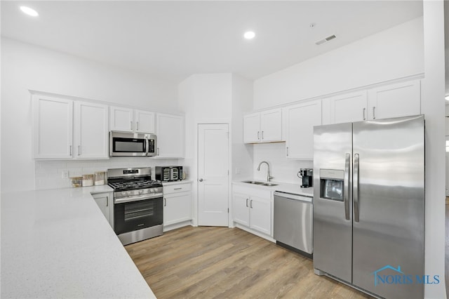 kitchen with backsplash, light wood-type flooring, appliances with stainless steel finishes, and white cabinetry