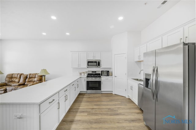 kitchen with stainless steel appliances, kitchen peninsula, sink, white cabinets, and light hardwood / wood-style floors