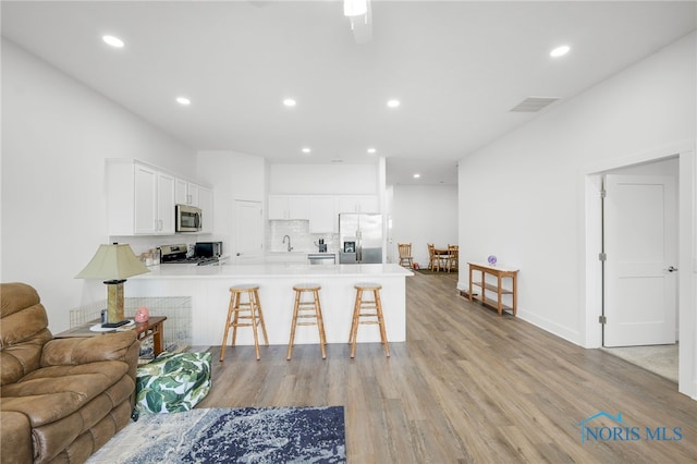 kitchen with a breakfast bar area, appliances with stainless steel finishes, kitchen peninsula, light wood-type flooring, and white cabinets