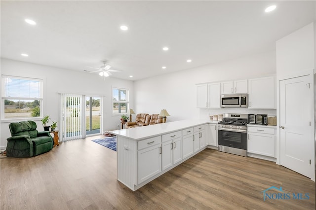 kitchen with light hardwood / wood-style flooring, kitchen peninsula, ceiling fan, appliances with stainless steel finishes, and white cabinets