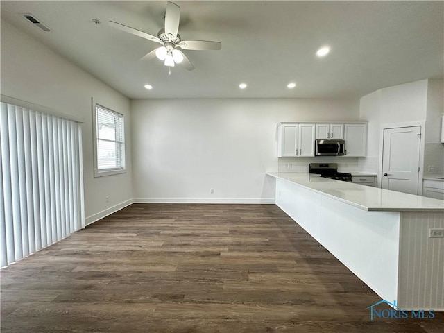 kitchen with tasteful backsplash, white cabinetry, dark hardwood / wood-style flooring, kitchen peninsula, and stainless steel appliances