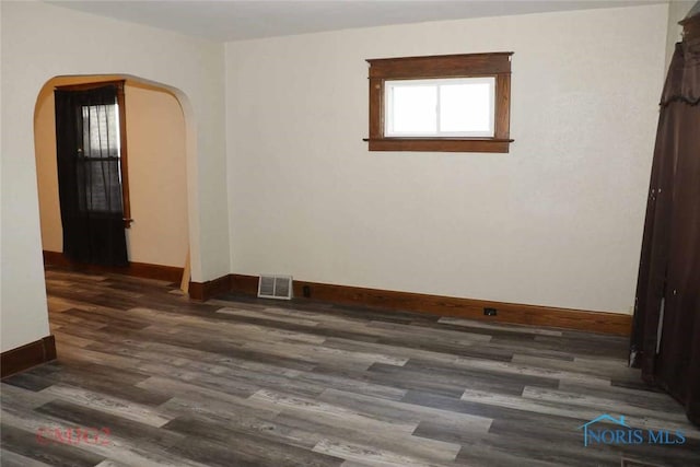 unfurnished room featuring visible vents, arched walkways, dark wood-type flooring, and baseboards