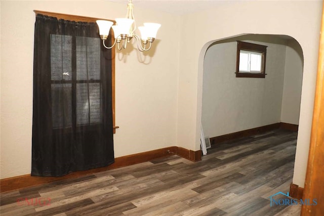 empty room featuring dark wood-type flooring and a notable chandelier