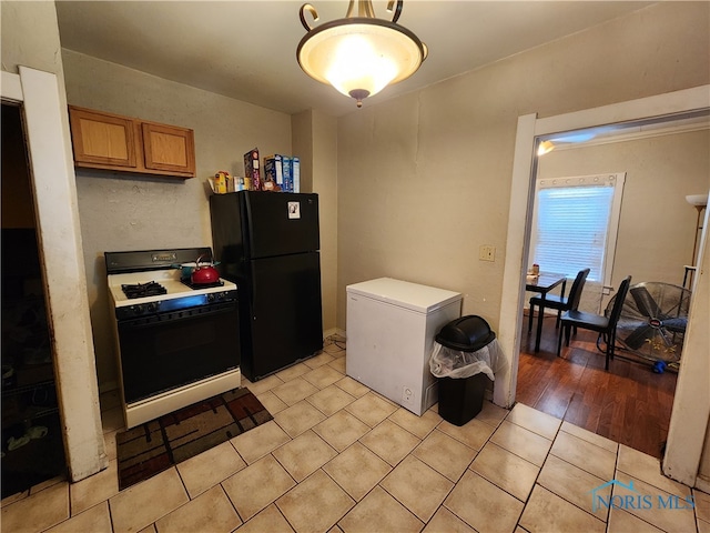 kitchen featuring light hardwood / wood-style flooring, refrigerator, white gas range, and black fridge