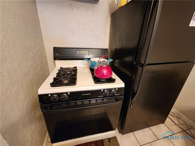 kitchen featuring light tile patterned floors, white gas range, and stainless steel fridge