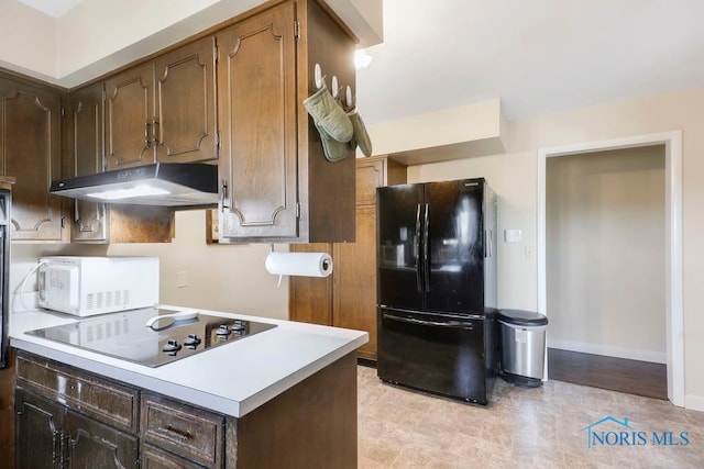 kitchen featuring cooktop, black fridge, and dark brown cabinets