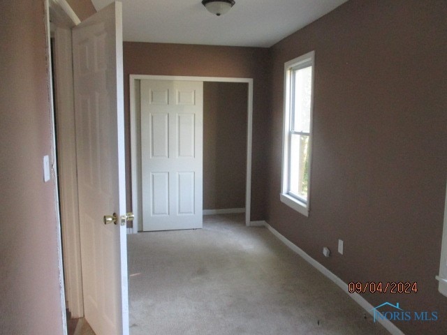 unfurnished bedroom featuring light carpet, multiple windows, and a closet